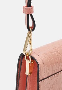 Rosa läderhandväska med präglade bokstäver, guldfärgad hårdvara och en avtagbar axelrem med svart accent. Slät textur och strukturerad form.