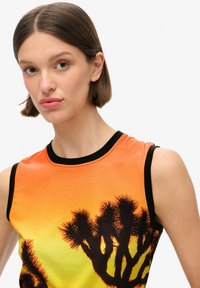 Top sin mangas con un degradado de naranja y amarillo, que presenta una silueta negra de palmeras. Cuello y sisas acanalados en negro.