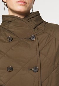 Hnědé prošívané svrchní oblečení s vysokým límcem, které má dva velké tmavé knoflíky a hladkou texturu. Žádné viditelné vzory nebo akcenty.