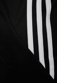 Il tessuto sportivo nero presenta tre strisce bianche lungo il bordo, con una superficie testurizzata e un collo a V.