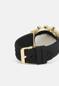 Schwarzes Gummi-Uhrenarmband mit strukturiertem Oberflächen, ausgestattet mit einer goldenen Metallschnalle und einem polierten goldenen Uhrgehäuse.
