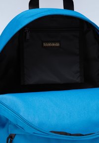 Zaino blu con una texture liscia, dotato di una tasca interna nera e un'etichetta. La cerniera è decisamente posizionata nella parte superiore, garantendo un facile accesso.