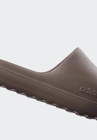 Brown slip-on sandal made of rubber with a smooth texture, rounded toe, and logo detail on the side. Features a ridged outsole for grip.