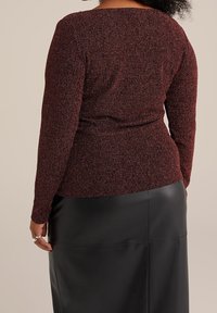 Top a maniche lunghe in maglia a costine bordeaux con scollatura ampia, abbinato a una gonna a tubino in pelle nera. Il tessuto testurizzato aggiunge interesse visivo.