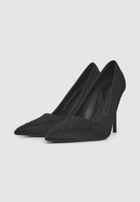 Talons aiguilles noirs avec des pointes, ornés de rhinestones noirs texturés. Doublure intérieure lisse et talons fins et hauts.