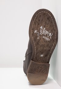 Chaussure en suede marron avec une tige texturée, dotée d'un talon en bois, de coutures blanches et d'un logo imprimé sur la semelle. Taille 37.
