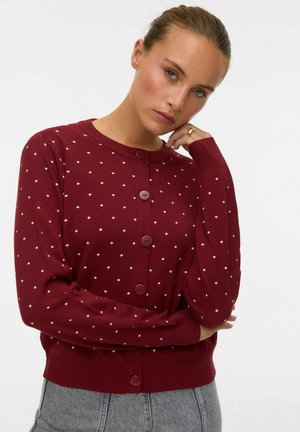 Cardigan bordeaux avec de petits pois blancs, col rond, manches longues et cinq boutons à l'avant. Tissu en tricot doux et ourlet côtelé.