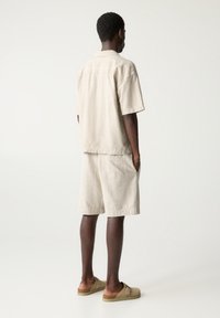 Linnen overhemd met korte mouwen in lichtbeige, gecombineerd met beige shorts en beige slip-ons. Heeft een relaxte pasvorm en zijzakken.