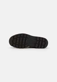 Semelle de chaussure en caoutchouc noir avec un motif de grip texturé et un bout arrondi. Comprend des marquages de marque et de taille.