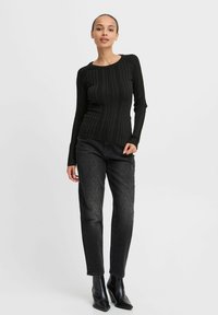 Svart ribbad långärmad topp med rund halsringning, i kombination med mörka jeans med subtila texturer. Modellen bär svarta ankelstövlar.