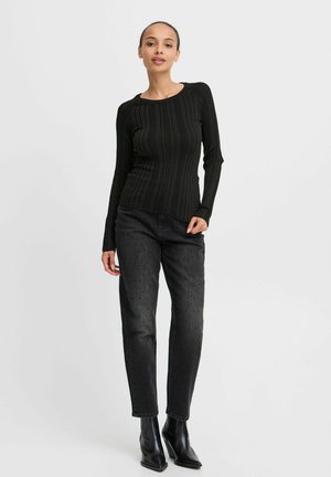 Svart ribbad långärmad topp med rund halsringning, i kombination med mörka jeans med subtila texturer. Modellen bär svarta ankelstövlar.