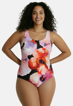 Hymyilevä nainen, jolla on pitkät kiharat hiukset ja joka pukeutunut hihattomaan yhden palan uimapukuun, jossa on suuret vaaleanpunaiset, punaiset ja violetit kukkakuviot.