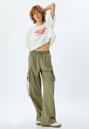 Witte cropped t-shirt met rode tekst "BETTER THAN YESTERDAY" in combinatie met lichtgroene cargo pants met zijzakken en een elastische tailleband.