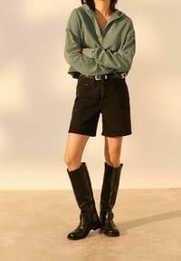 Groene cropped hoodie, zwarte denim shorts en kniehoge zwarte leren laarzen. Gladde textuur met ingetogen ontwerpen en geen zichtbare patronen.
