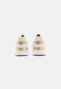 Scarpe sportive bianche con una superficie liscia, caratterizzate da un accento dorato e un tallone imbottito per il massimo comfort. Schiena rinforzata e branding minimale.