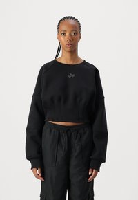 Svart avkortet sweatshirt med brede ermer, teksturert materiale og subtilt frontlogo. Kombinert med løse svarte cargo-bukser med lommer.