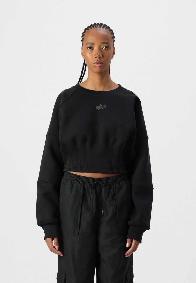 Svart avkortet sweatshirt med brede ermer, teksturert materiale og subtilt frontlogo. Kombinert med løse svarte cargo-bukser med lommer.