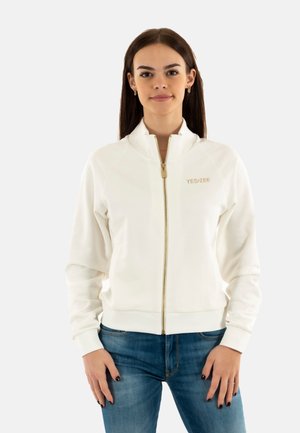 Felpa bianca con zip e collo alto, zip dorata e logo "YES-ZEE" sul petto. Tessuto morbido con polsini e fondo a costine.