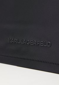Černá textilie s hladkým povrchem, zdobená vyraženým logem "KARL LAGERFELD". Švy jsou úhledné a rovnoměrné podél okraje.