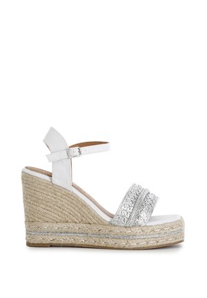 Sandalia de cuña blanca con plataforma de yute trenzado, tira frontal trenzada plateada y correa ajustable en el tobillo con hebilla.