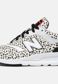 Baskets blanches avec un motif à taches noires, dotées d'une tige en cuir et textile. Comprend des lacets noirs et une semelle intermédiaire blanche ; logo "N" proéminent.