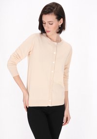 Cardigan lung, de culoare bej deschis, realizat dintr-un material tricotat moale. Are un guler rotund și șapte nasturi pe față, cu manșete și tiv cu model în relief.