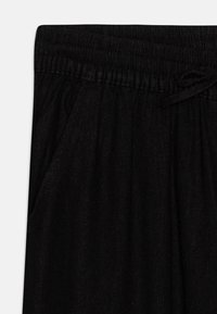 Pantaloni jogger neri con vita elasticizzata, dettagli con lacci e tasche laterali. Il tessuto presenta una finitura morbida e texturizzata.