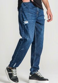 Modré džíny z denimu s úchvatnými detaily a trhlinami, které mají volný střih a šité švy, spárované s černobílými teniskami.