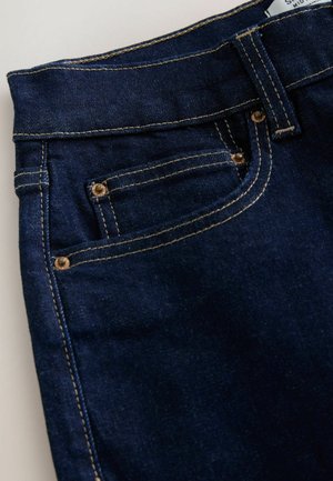 Tumed sinised teksad, millel on sobiv vöökoht, kontrastne kuldne tikkimine ja eesmine tasku, millel on metallnööpide detailid.