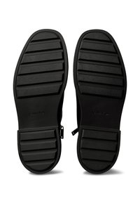Czarne buty z teksturowanymi gumowymi podeszwami; posiadają poziome rowki dla lepszej przyczepności. Wytłoczone logo "Calvin Klein" w okolicy pięty. Gładki materiał cholewki.