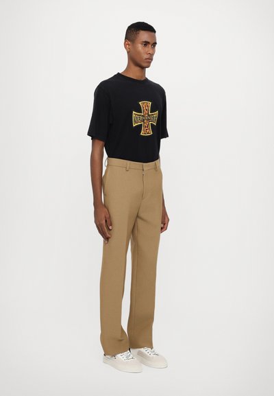 Maglietta nera con una grafica a croce colorata, abbinata a pantaloni beige a gamba dritta e sneakers bianche. Design semplice e casual.