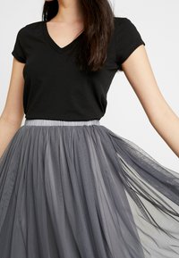 Zwarte V-hals t-shirt gecombineerd met een grijze tule rok met gelaagde, doorzichtige stof en een elastische tailleband.