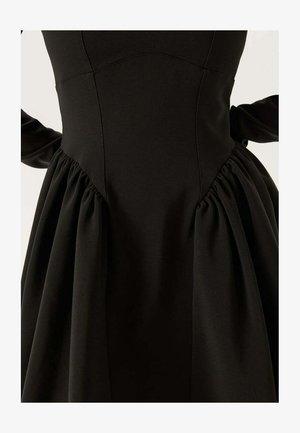 Robe noire avec un corsage ajusté à coutures verticales et une jupe froncée. Le tissu a une texture lisse et une légère brillance.