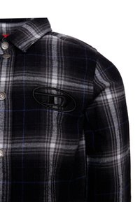Camicia a quadri bianca e nera con accenti blu, caratterizzata da un colletto con bottoni e una toppa con logo ricamata sul lato sinistro del petto.
