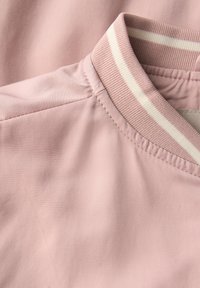 Tissu rose clair à la texture lisse avec un col à motif rayé crème et blanc. Gros plan sur les détails de couture et du col.