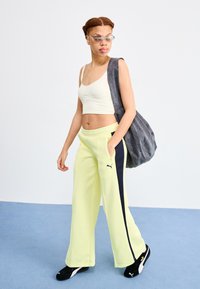 Light yellow sweatpants with navy side stripes, a fitted cream top, and gray shoulder bag. Black sneakers complete the sporty outfit.