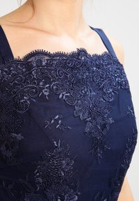 Marinblå klänning med en texturerad, broderad överdel med blommönster, intrikata detaljer och smala axelband.