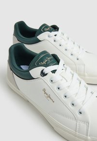 Baskets en cuir blanc avec des détails et un logo verts. Présentent une langue et des lacets texturés, une forme arrondie et une semelle en caoutchouc plate.