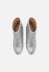 Botines plateados con brillo, de superficie suave y cremallera lateral. Diseño de punta redonda y forro interior beige.