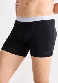 Boxer briefs SLOGGI neri con elastico grigio in vita. Texture liscia, design aderente e aperture delle gambe che si estendono fino a metà coscia.