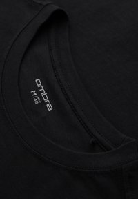 T-shirt noir à col rond avec une étiquette de marque visible indiquant « ombre EUR M 48 » à l'intérieur du col. Tissu lisse avec coutures détaillées.