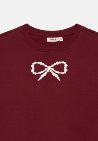 Mörk röd tröja med ett vitt pärlmönster av en slinga på framsidan. Halsringningen är ribbad. Märket är "ONLY." Mjuk textur.