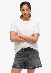T-shirt en coton blanc à manches courtes, associé à un short en jean noir avec un ourlet effiloché et une ceinture noire avec une boucle en argent.