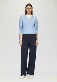 Hellblaues V-Neck-Pullover, lange Ärmel, kombiniert mit marineblauen weit geschnittenen Hosen und weißen Sneakers. Weicher Stoff, lockere Passform, minimalistisches Design.