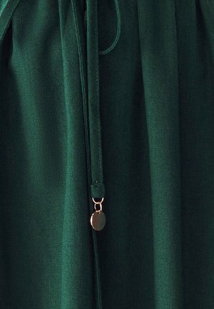 Zielony materiał o gładkiej fakturze, z zapięciem na sznurek oraz akcentem w złotym odcieniu.