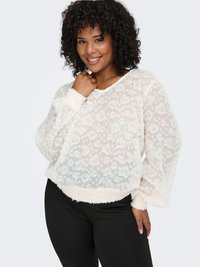 Vit, genomskinlig tröja med blommönster och långa ballongärmar; har ribbad, elastisk fåll och muddar. Bärs med svarta leggings.