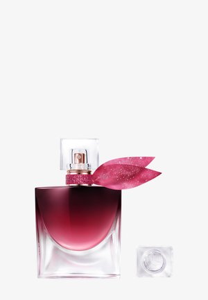 Quadratische Parfümflasche mit verlaufender dunkelrosa Flüssigkeit, klarem Verschluss und zwei rosafarbenen glitzernden blattförmigen Verzierungen neben der Sprühdüse.