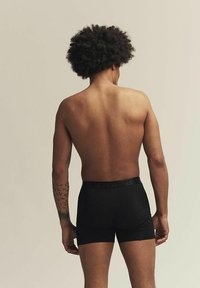 Boxers ajustados negros con una cintura de logotipo, diseño ajustado, tela suave y sin patrones visibles; modelo mostrado desde la parte de atrás.
