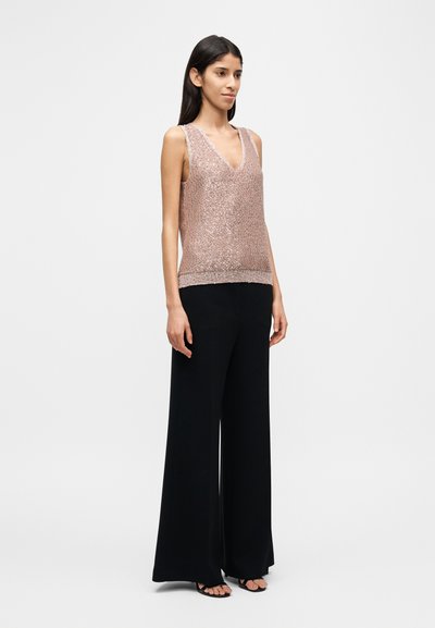 Τοπ με λουράκια από ροζ χρυσό παγιέτα με V-λαιμόκοψη και ριμπ τελείωμα, συνδυασμένο με μαύρο παντελόνι πλατύ πόδι και μαύρα σανδάλια. Απλή, μοντέρνα σιλουέτα.