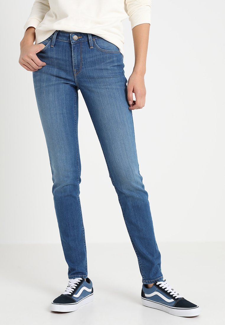 Narrowa blå jeans med ljus tvätt, femfickors design, knappstängning fram och subtila blekningar. Matchas med marinblå sneakers.